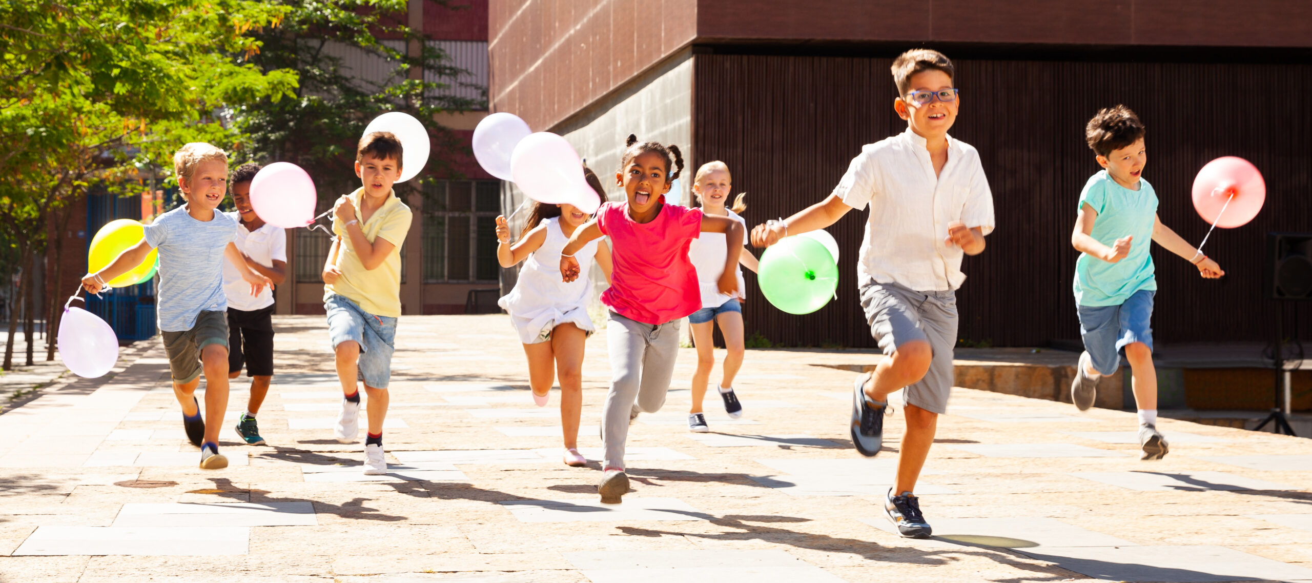 Niños felices con globos corren en la calle de la ciudad de verano
